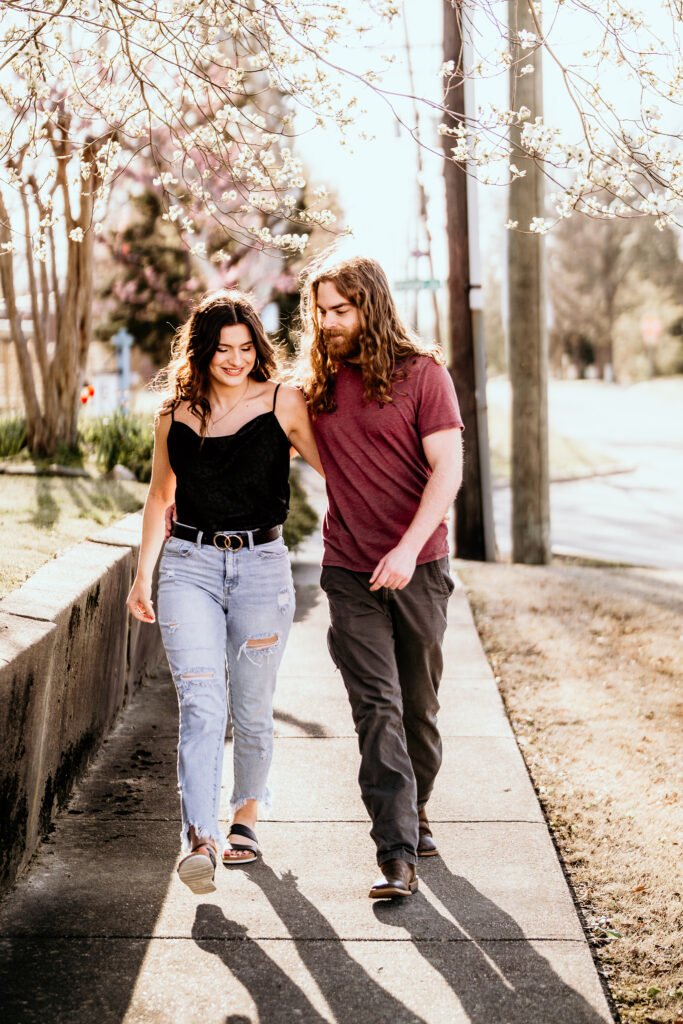 Couples walking toward the camera under a blooming tree backlit by a warm sunny glow for their engagement session