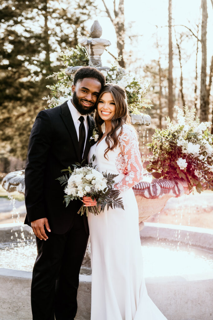 Bride and groom at sunset standing in front of a beautiful water fountain decorated with florals