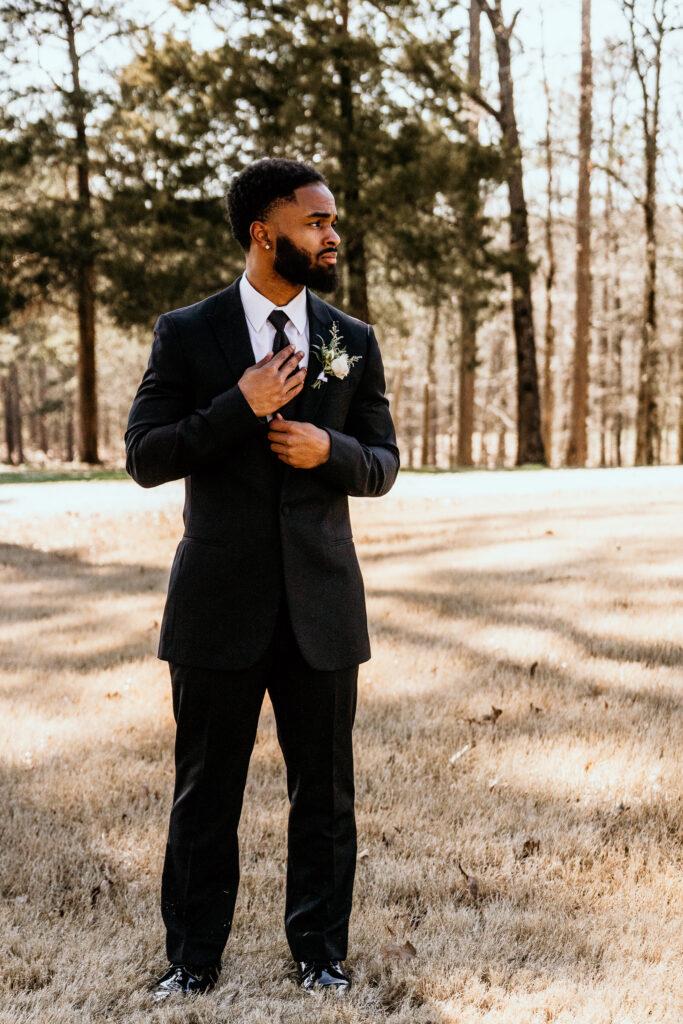 Groom adjusting tie while looking into the distance in anticipation of what is to come