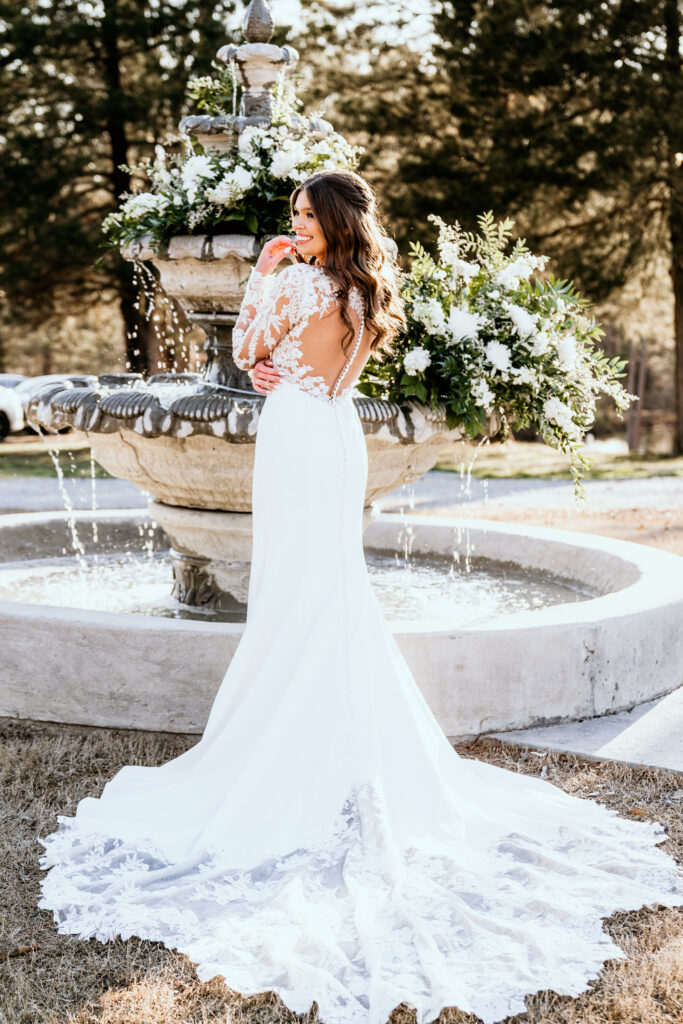 Back shot of the bride capturing the button and lace details of the dress in front of the floral decorated water fountain