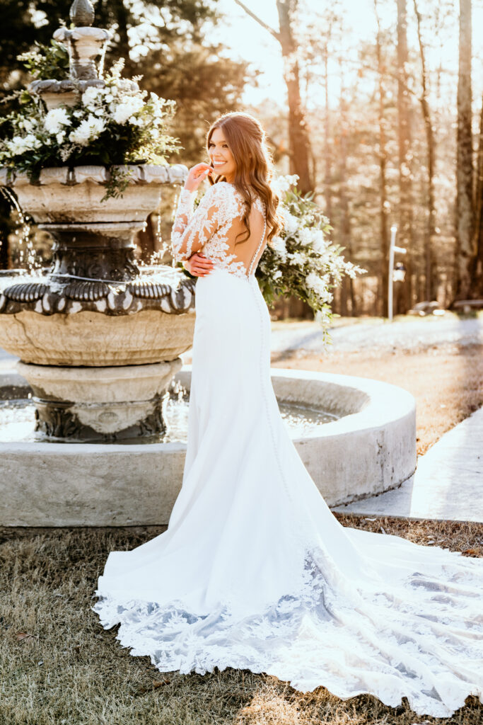 Side shot of the bride capturing the button and lace details of the dress in front of the floral decorated water fountain surrounded by the glow of the setting sun