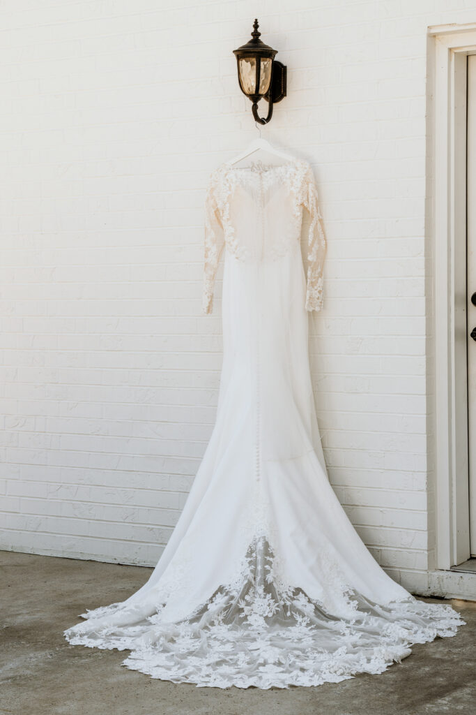 Wedding dress hanging from a light fixture to show the lace and button details before the bride is in the dress