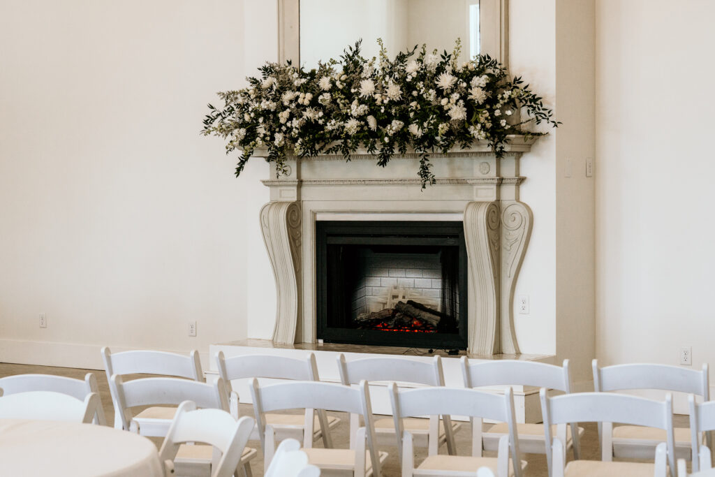 Fireplace with florals set for a ceremony surrounded by white chairs