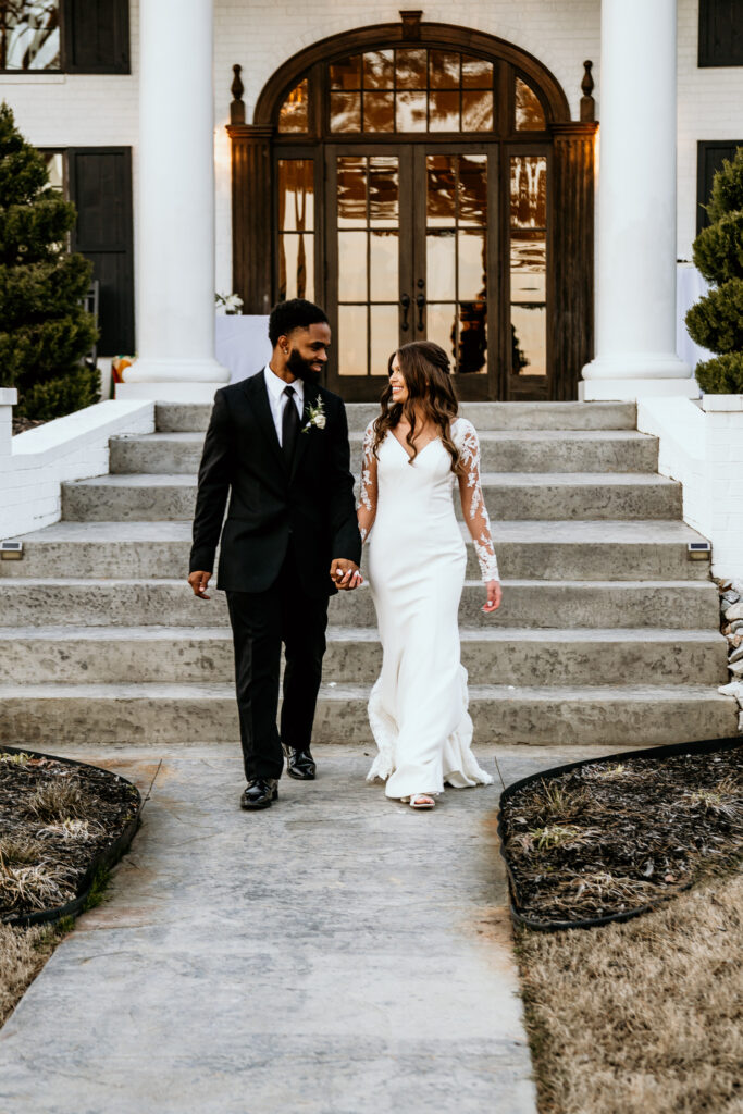 Bride and groom walking away from their venue at dusk holding hands and smiling