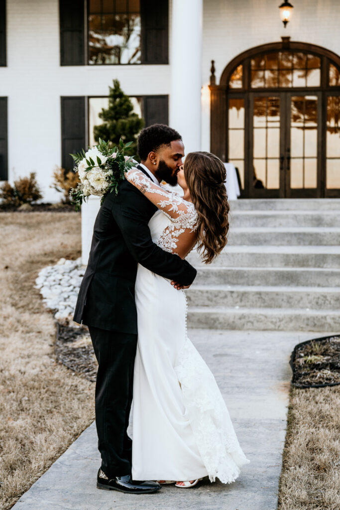 The bride and groom share a kiss in front of their venue for a moment along at dusk