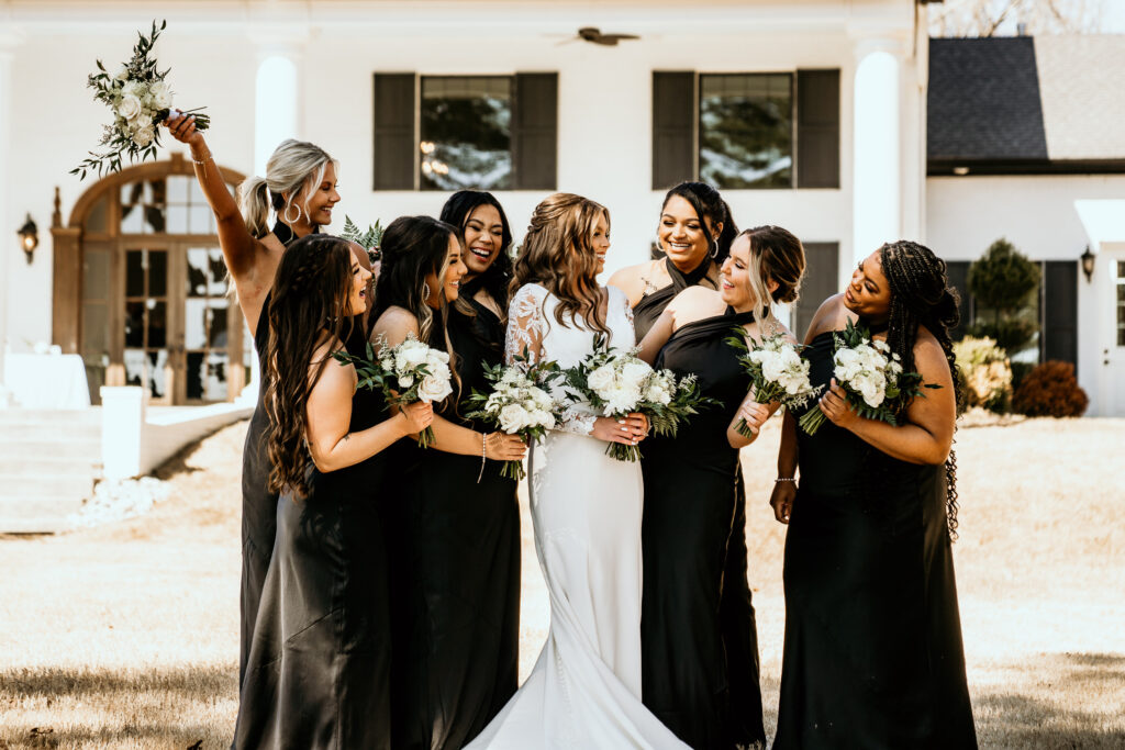 Bride and her bridal party laughing at each other in front of the wedding venue