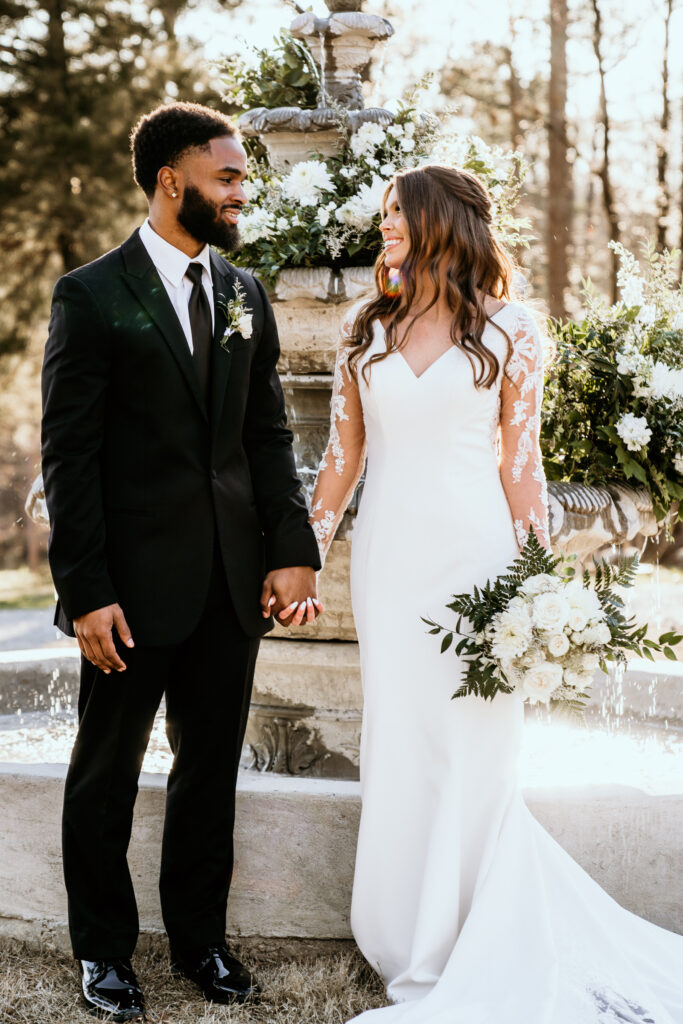 Bride and groom share a look at each other while holding hands in front of the water fountain 