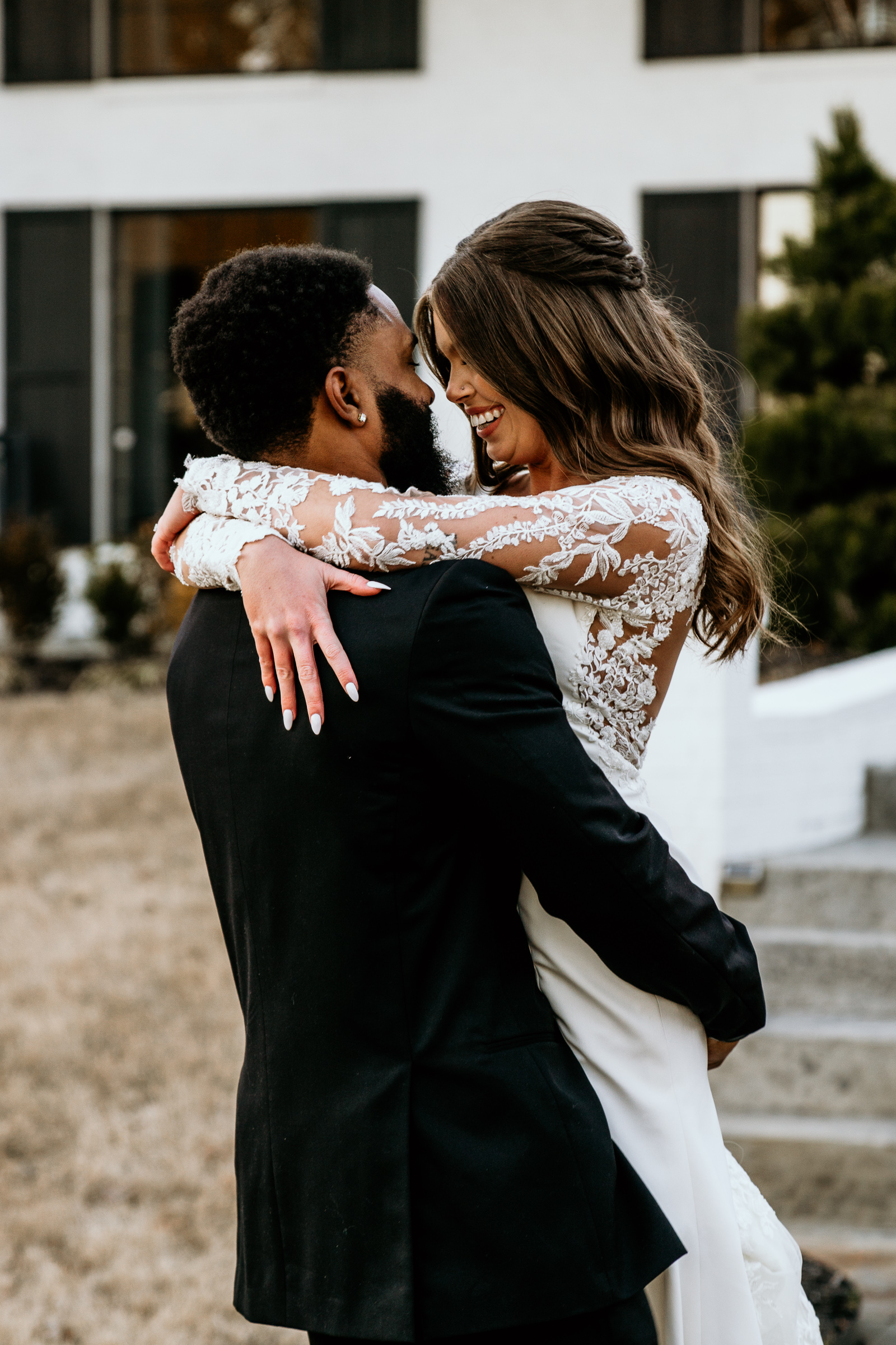 Still holding his bride, the groom leans in closer nose-to-nose with his smiling bride