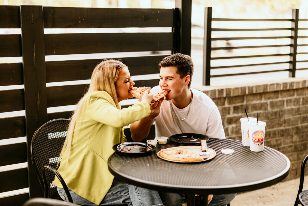 couple biting into a shared pizza for their engagement session