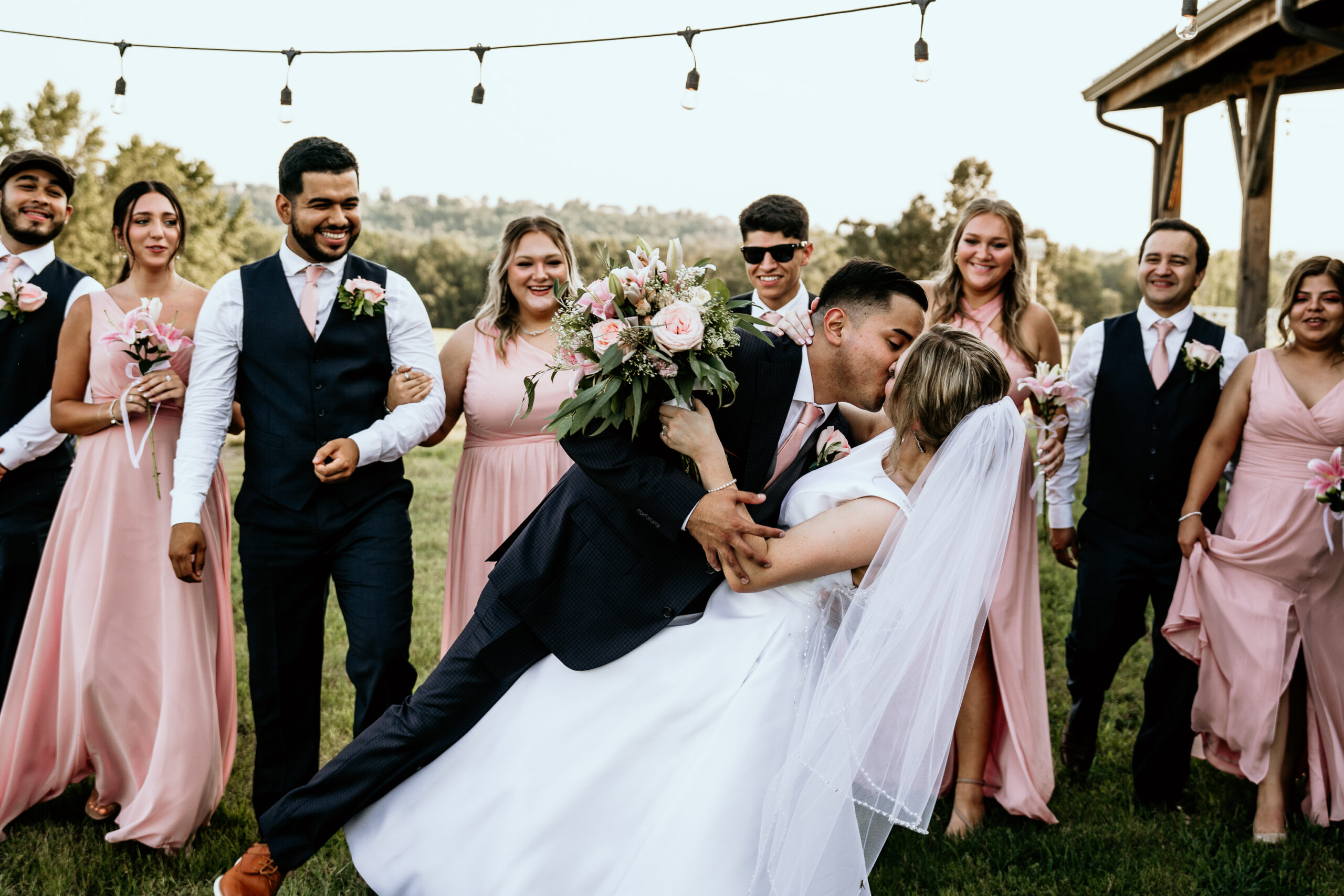 the groom dips the bride for a kiss in front of the cheering wedding party